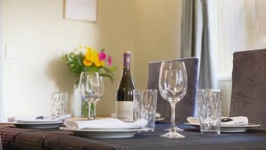 A dining table set with plates, glasses, and a bottle of wine, with a vase of flowers and a framed sign in the background. - RIMA | Sun-Soaked Hideaway (Queenstown)