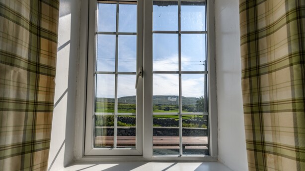 Ein Fenster mit Blick auf eine grüne Landschaft und eine Steinmauer.