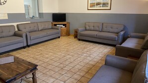 Ein Wohnzimmer mit zwei grauen Sofas, einem Holztisch, einem Fernseher und einem gerahmten Landschaftsbild an der Wand.