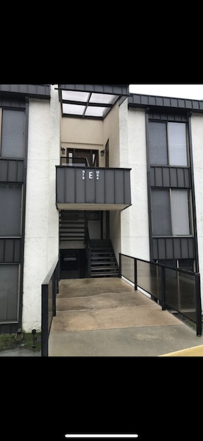 Een modern gebouw met een centrale trap, een balkon en een bord met de letters 'E' en de cijfers '73' en '24'.