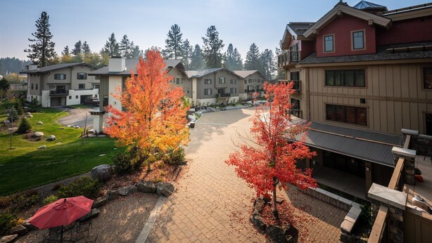 A residential area with multiple two-story houses, a paved driveway, and autumn-colored trees.