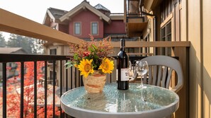 A round glass table with a bottle of wine and a glass on it, a vase with sunflowers, and a chair.