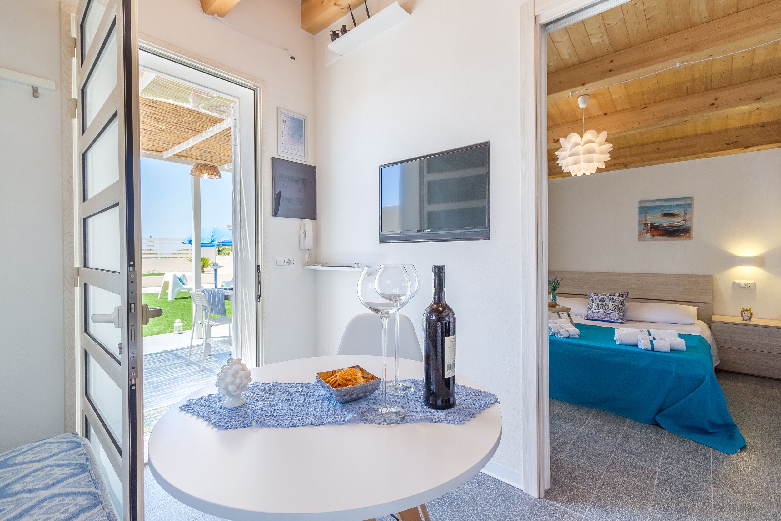 A room with a bed, a TV, a table with a wine bottle and glasses, and a view of the outdoors.