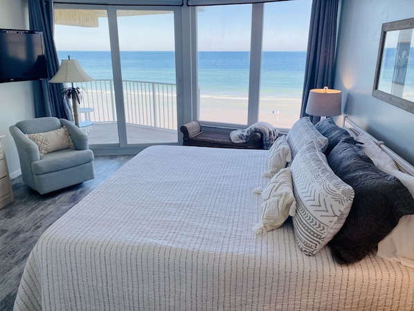 A bedroom with a large bed, a chair, a TV, and a view of the beach. - WEEKLY DISCOUNTS! DIRECT BEACH ACCESS! NO DRIVE BEACH! FULL KITCHEN! POOL! (Daytona Beach Shores)