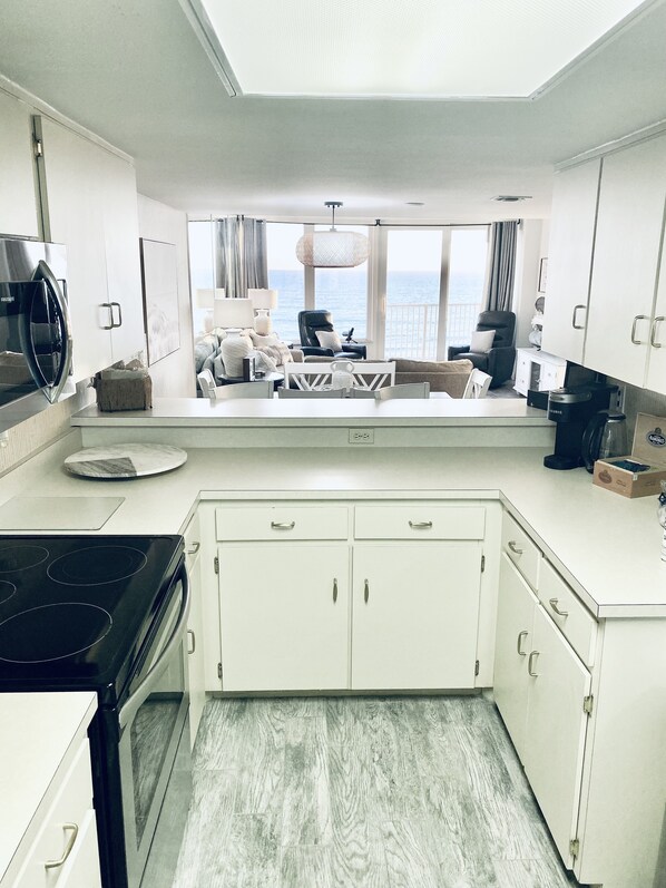 A modern kitchen with a view of the sea, white cabinetry, a stove, and a dining area with a view. - WEEKLY DISCOUNTS! DIRECT BEACH ACCESS! NO DRIVE BEACH! FULL KITCHEN! POOL! (Daytona Beach Shores)