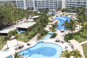 Ein Resort mit mehreren Swimmingpools, Palmen und einem großen Gebäude im Hintergrund.