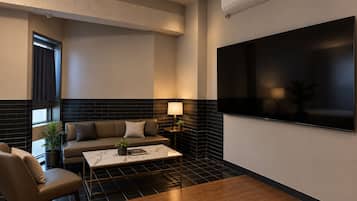 Un soggiorno moderno con divano, poltrona, tavolino e una TV a schermo piatto fissata al muro.