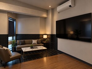 A modern living room with a sofa, armchair, coffee table, and a flat-screen TV mounted on the wall. - 648 Hotel (Seoul)