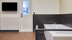 A bathroom with a black and white tiled wall, a white bathtub, and a mounted TV on the wall. - 648 Hotel (Seoul)