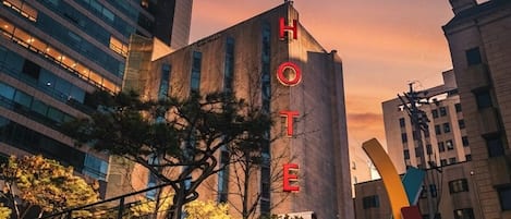 A hotel building with a prominent 'HOTEL' sign, surrounded by modern architecture and a staircase leading to the entrance.