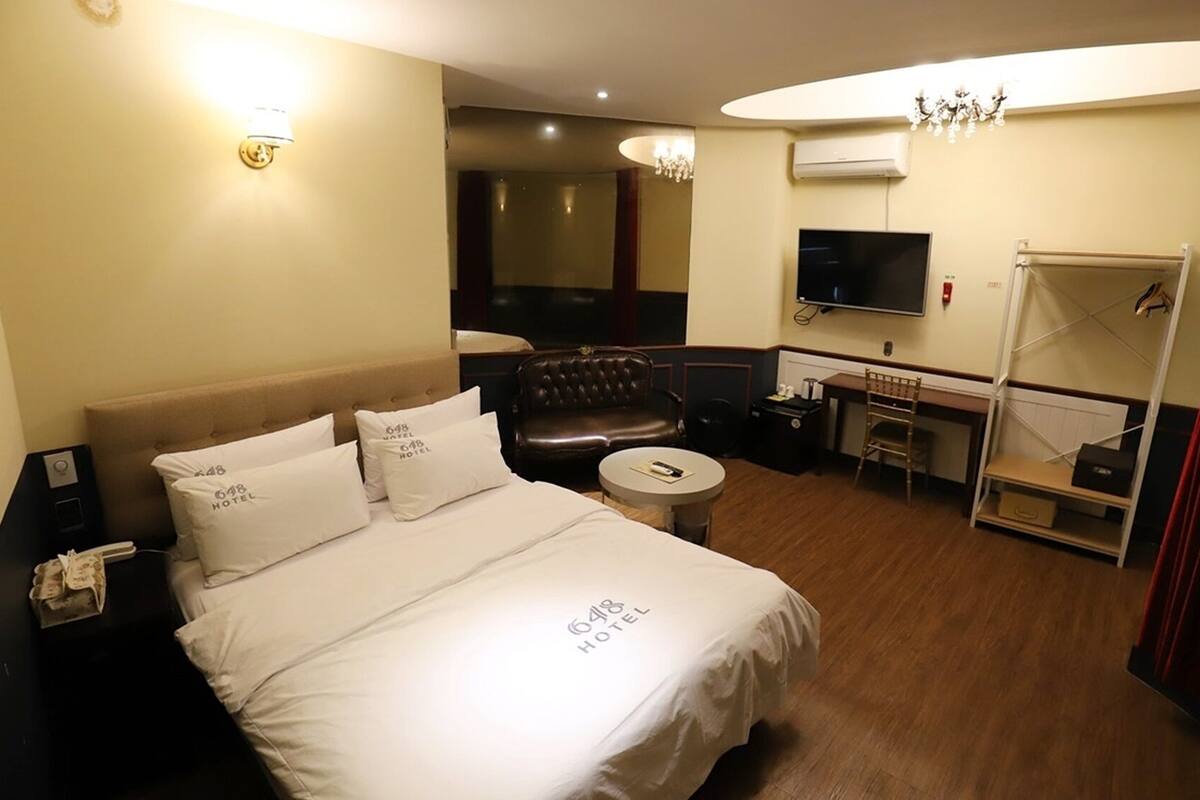 A hotel room with a bed, a desk, a chair, a TV, and a wardrobe.