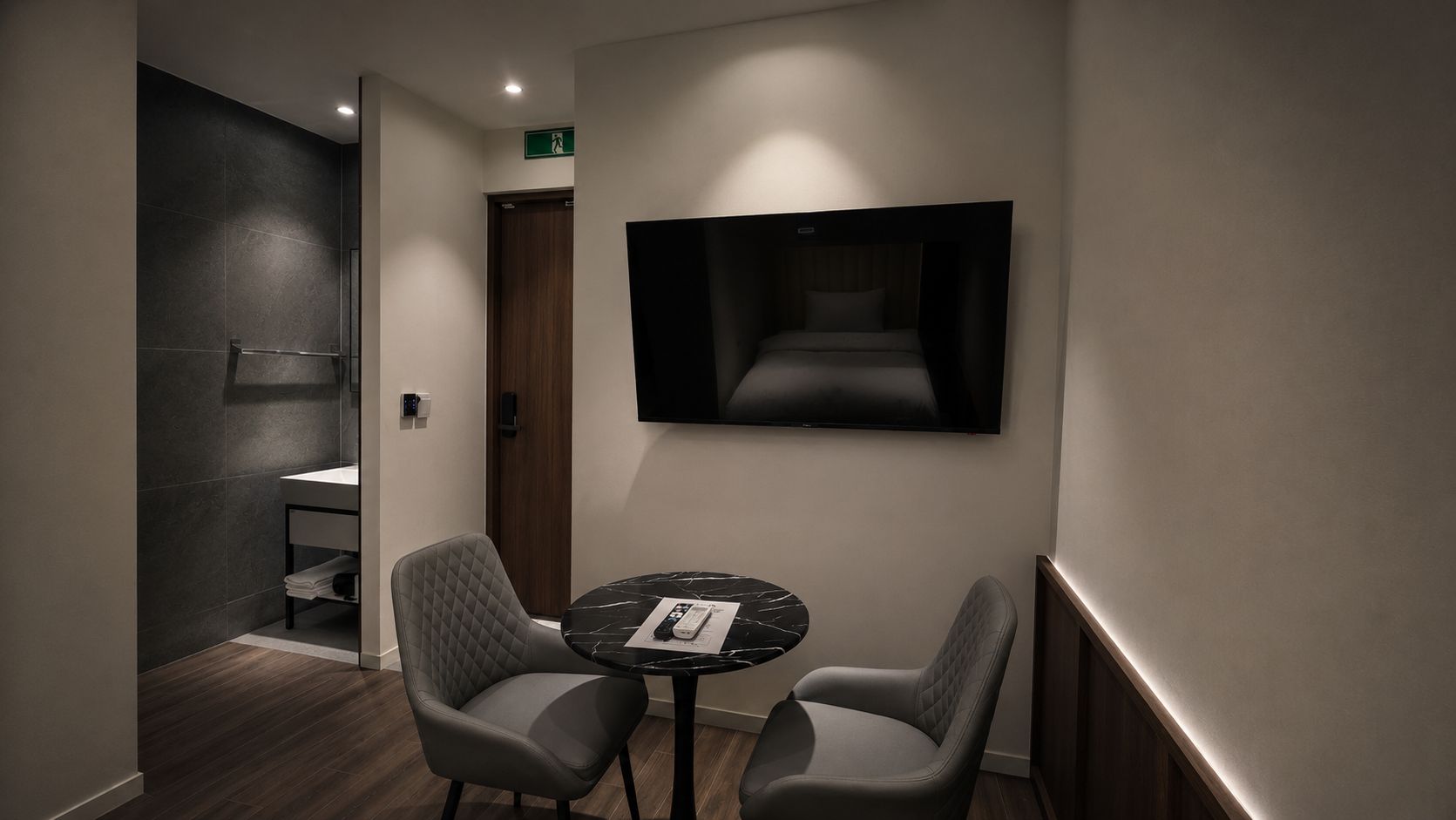 Habitació d'hotel amb un llit, una televisió penjada a la paret, una taula petita amb cadires i un bany amb un lavabo i un vàter.