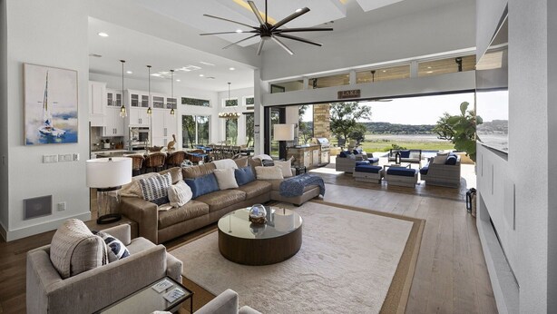 A spacious living room with a large sectional sofa, a coffee table, and a view of a lake. - Whispering Waters - Lakefront Luxe, Pool + Hot Tub + Fire Pit + Outdoor Kitchen + 2 Master Suites (Canyon Lake)