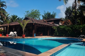 A swimming pool with a tiled edge, surrounded by potted plants and outdoor furniture. - Pousada Baobá (São Sebastião)