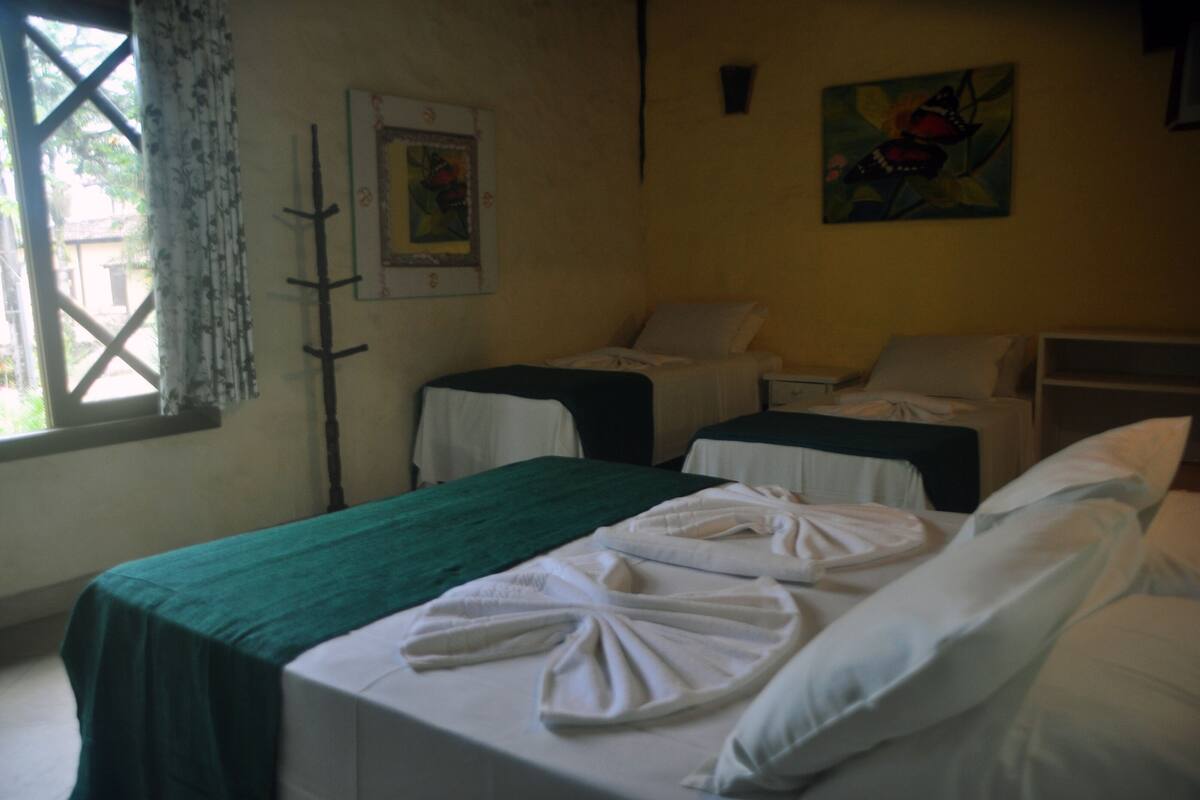 Une chambre d’hôtel avec deux lits, une couvre-lit verte, du linge de lit blanc, une fenêtre avec vue et des œuvres d’art accrochées aux murs.