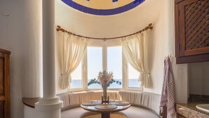Un rincón con asientos y vistas al mar, una mesa redonda con un florero, y un armario de madera.