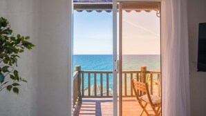 Una habitación con puerta de vidrio corrediza que da a un balcón con terraza de madera y una silla.