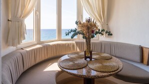 Un rincón con asientos, una mesa redonda, un jarrón con flores secas y vistas al mar a través de amplios ventanales.