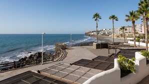 Un paseo marítimo con vistas al mar, palmeras y un edificio al fondo.