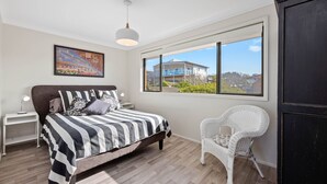 A bedroom with a bed, a chair, a nightstand, a lamp, a window, and a painting. - Montague Views Kianga (KIANGA)