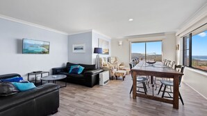 A spacious living area with a black leather sofa, a dining table with chairs, and a view of the ocean through large windows. - Montague Views Kianga (KIANGA)