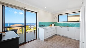 A modern kitchen with a view of the sea, white cabinets, a green tiled backsplash, and a sliding glass door leading to a balcony. - Montague Views Kianga (KIANGA)