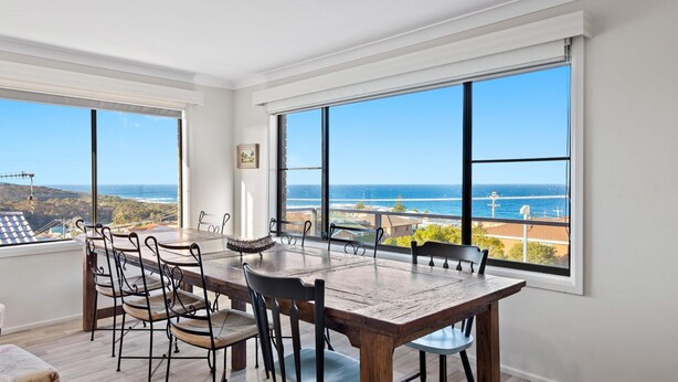 A dining area with a large table and chairs, large windows with a view of the ocean and hills. - Montague Views Kianga (KIANGA)