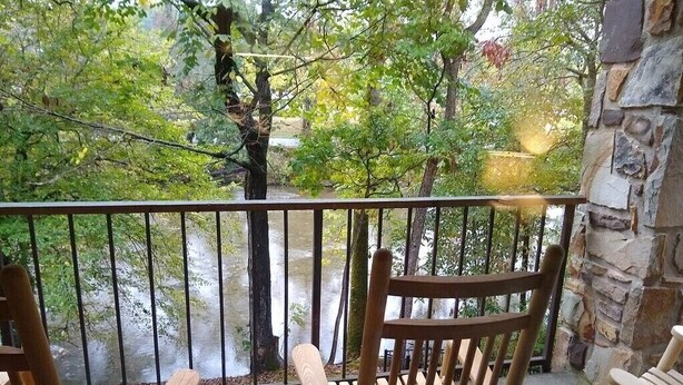 Eine Holzterrasse mit zwei Schaukelstühlen, die auf einen Fluss mit Blick auf Bäume und Steinmauern blickt.
