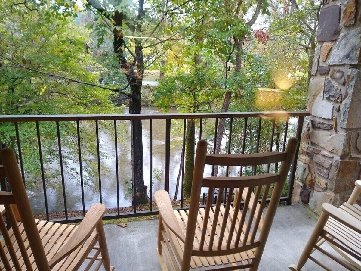 Rocking chairs on Riverside Condo in Townsend, overlooking the river through green leaves of tall trees.