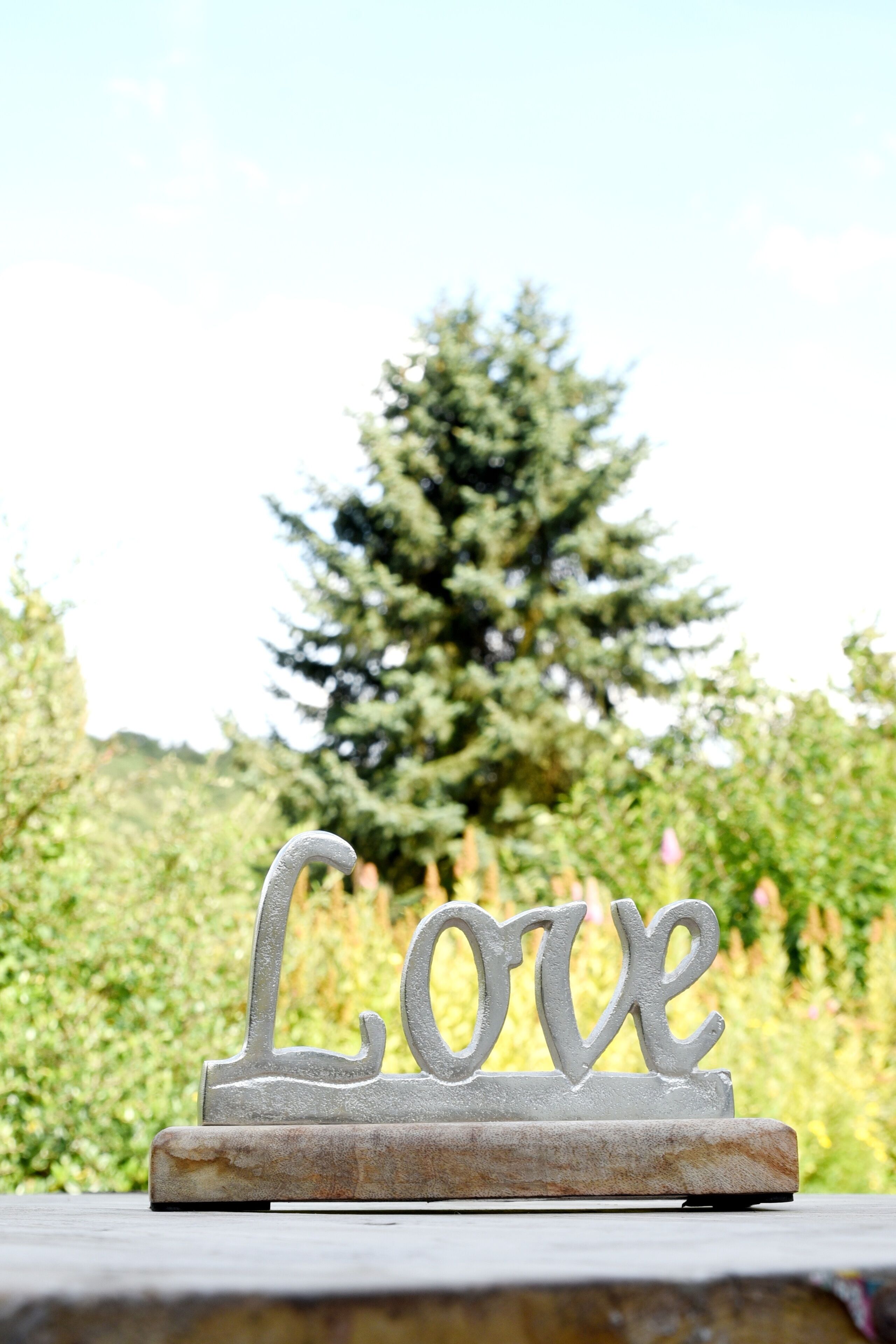 A stone plaque with the word "Love" on it, placed outdoors with a backdrop of greenery and a tree.