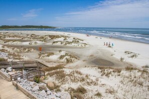 Une plage avec des dunes, une promenade en bois et une côte visible au loin.