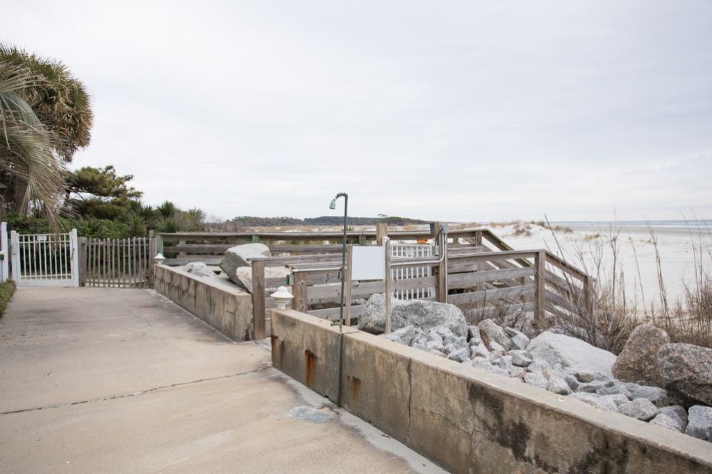 A concrete pathway leading to a wooden bridge over a rocky area with a view of the water.
