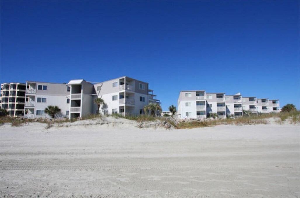 Un hotel frente a la playa con edificios de varios pisos, balcones y una playa arenosa al frente.