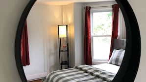 Een slaapkamer met een bed, nachtkastje, lamp en een raam met gordijnen.