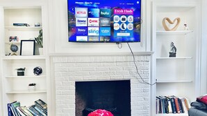 Een woonkamer met een flatscreen-televisie die boven een witte bakstenen schoorsteen is bevestigd, omringd door boekenkasten en een salontafel met een bloevas.