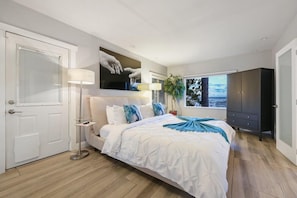 A bedroom with a bed, bedside table, lamp, and a large window with a view.