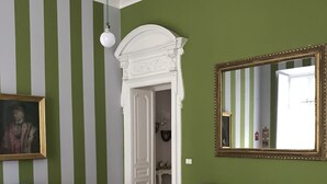 A living room with green and white striped walls, a white fireplace, a grey sofa with patterned cushions, a red armchair, and a round coffee table with red legs. - The best B&b in town (Torino)