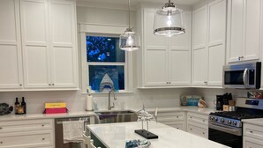 Une cuisine moderne avec des meubles blancs, un îlot central, un évier en acier inoxydable et un four à micro-ondes.