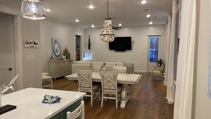 Un coin repas avec une table blanche, des chaises et un lustre. Un téléviseur est fixé au mur, et une pancarte indique « Quintin Cottage ».