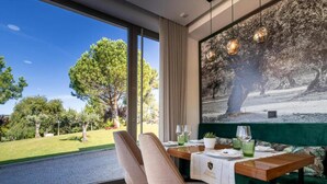 A dining area with a view of a garden, a table set with a tablecloth, chairs, and a green sofa. - Olive Nature - Hotel & SPA (Valpacos)