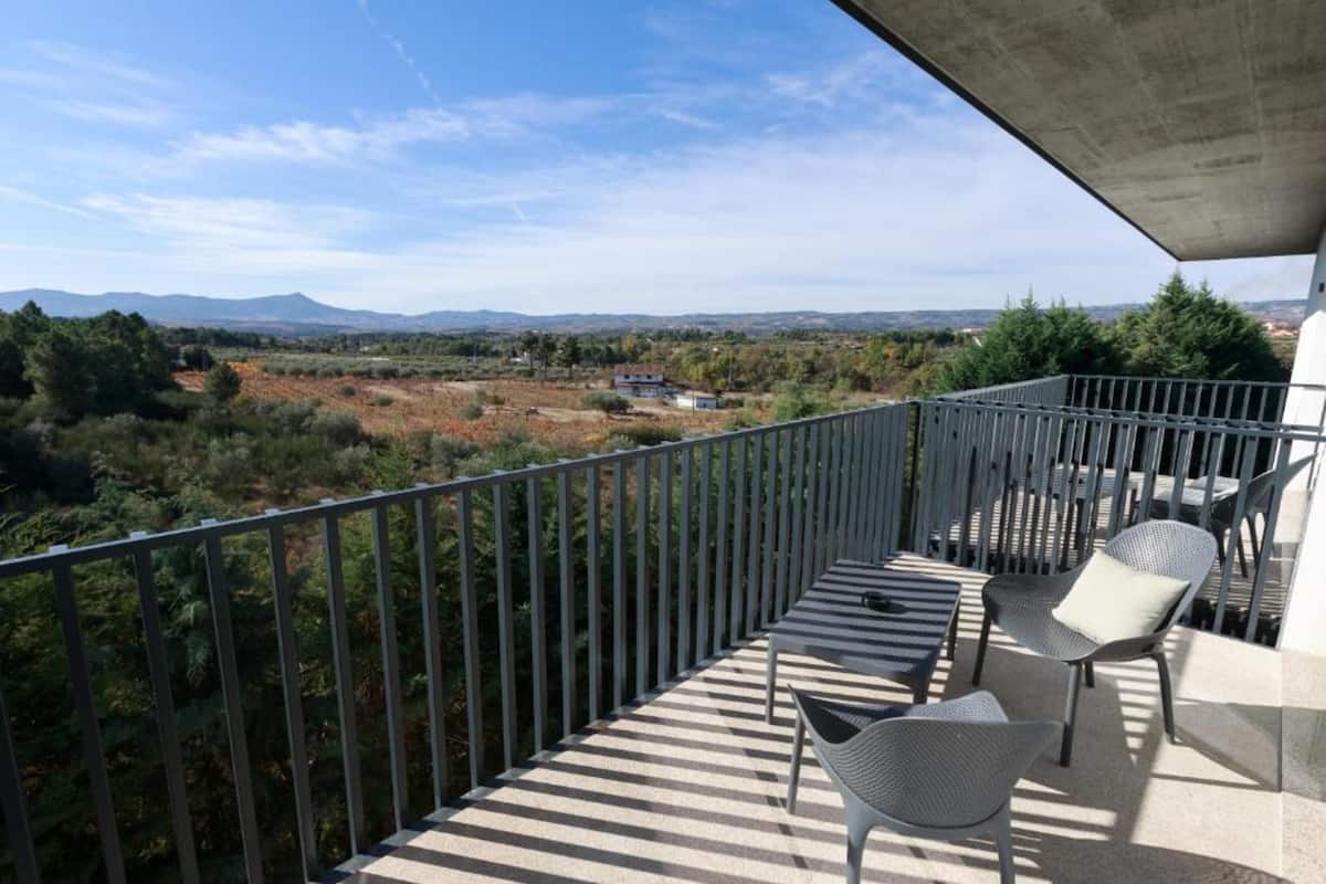 A balcony with a view of a rural landscape, a table, and two chairs.
