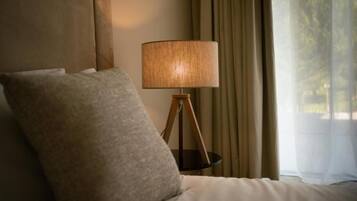 A bed with a single pillow, a bedside lamp on a wooden stand, and a window with curtains.