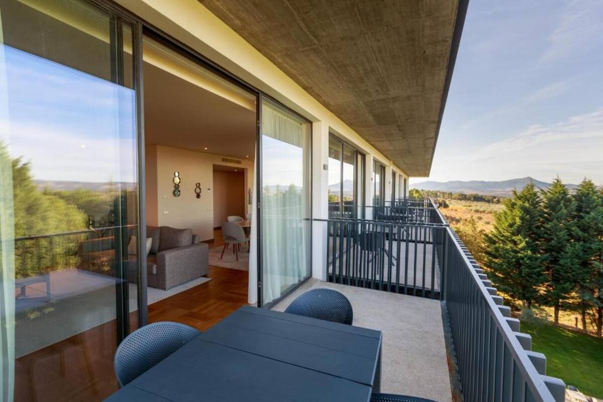 A balcony with a view of the countryside, a dining area with a table and chairs, and a living room with a sofa and a coffee table.