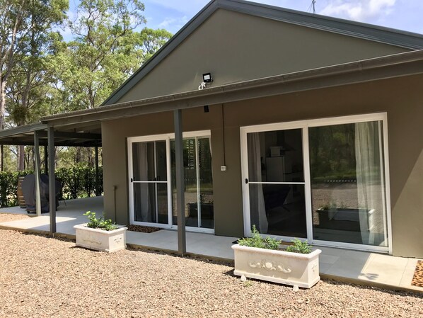 A modern building with large sliding glass doors, a covered porch area, and outdoor planters. - Tucked away in the Heart of the Hunter valley (North Rothbury)