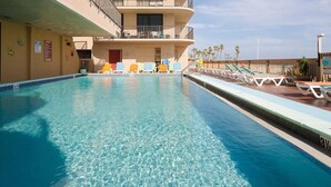 Une piscine avec des chaises longues et un bâtiment doté de balcons.