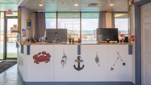 Un comptoir d’accueil avec vue sur la mer, une décoration en forme d’ancre portant l’inscription « Bienvenue » et un panneau « Il est interdit de fumer ».