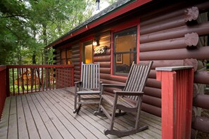 Une cabane en rondins dotée d’une terrasse, de deux fauteuils à bascule et d’une fenêtre sur laquelle est affiché le numéro 223.