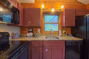 Una cocina con gabinetes de madera, encimera de granito, microondas, tostadora, cafetera y refrigerador.