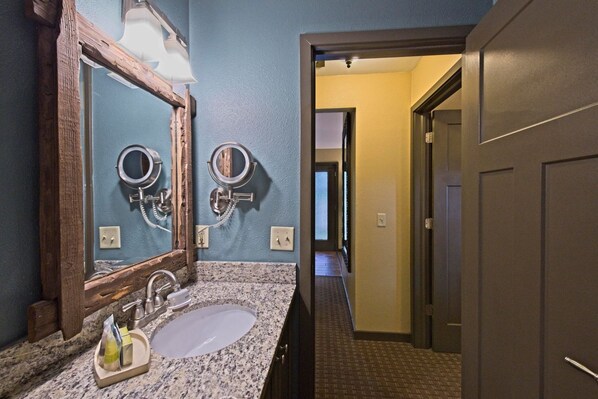 Une salle de bain avec un comptoir en granit, un lavabo, un miroir et deux porte-serviettes.