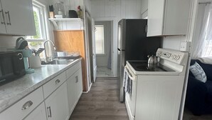 A compact kitchen with white cabinets, a stainless steel refrigerator, and a built-in oven. - Quaint Cottage Vacation (Old Orchard Beach)